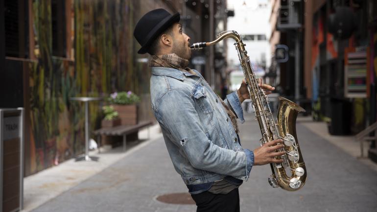 Omar Aragones playing the saxophone in The Belt, an alleyway filled with street art